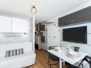 A modern kitchen with a built-in TV, a dining area with a white table and chairs, and a cozy seating area with a striped pillow.