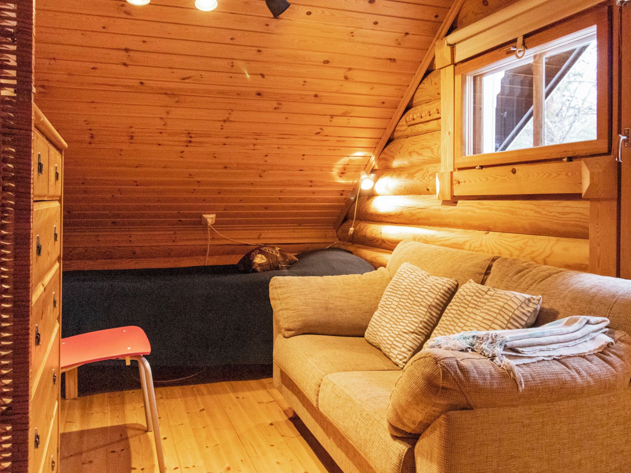 A cozy cabin interior with a wooden ceiling, a sofa with cushions, a small table, and a window.