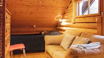 A cozy cabin interior with a wooden ceiling, a sofa with cushions, a small table, and a window.