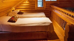 Een blokhut met twee bedden, een raam en een houten leuning.