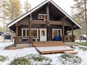 Une cabane en rondins avec un porche à l’avant, une porte et une petite fenêtre.