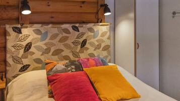 A bed with a leaf-patterned headboard, two pillows, and two wall-mounted lamps.