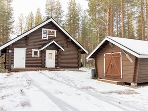 A cabin with a large door and a smaller door, both with white trim, and a separate shed with a wooden door.