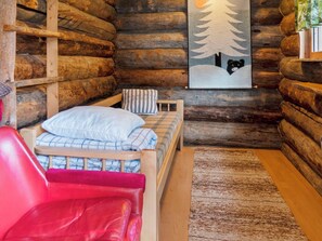 A cozy log cabin room with a bed, a red chair, and a wall-mounted painting. - Agenttimajat 1 by Interhome (Kuusamo)