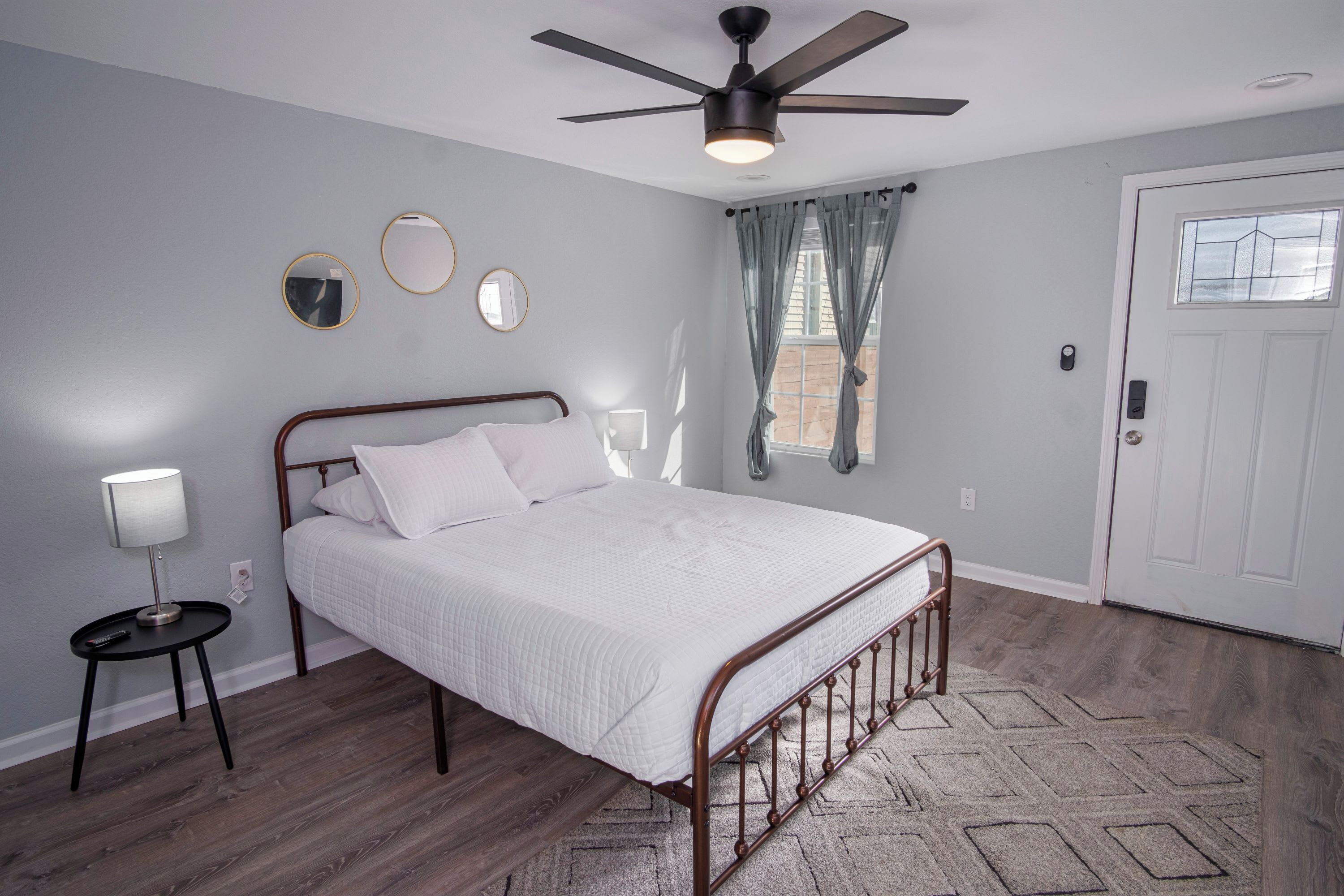 Une chambre à coucher avec un lit, une table de chevet, un ventilateur de plafond et une porte.