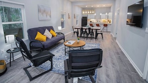 A modern living room with a sofa, chairs, a coffee table, and a dining area with a kitchen in the background.