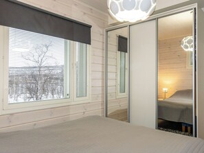 Une chambre à coucher avec un lit, une fenêtre avec des stores, un miroir et une porte donnant sur une autre pièce.
