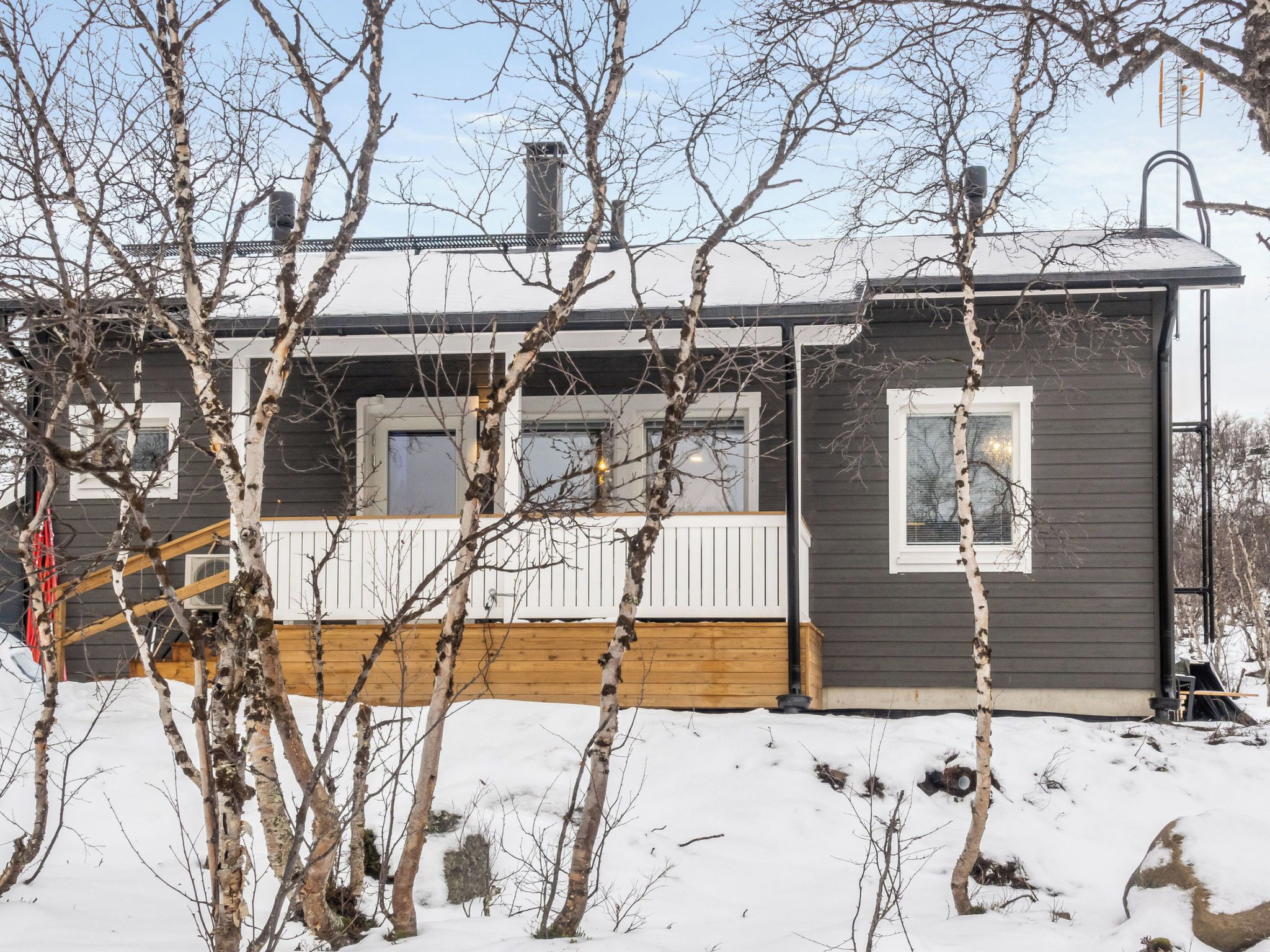 A cabin with a deck, a chimney, and a snow-covered ground.