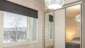 A bedroom with a bed, a window with blinds, a mirror, and a door leading to another room. - Willa kiiruna by Interhome (Enontekiö)