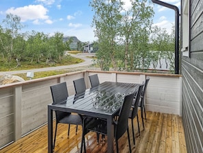 Un patio al aire libre con una mesa y sillas negras, rodeado por una terraza de madera y una cerca de metal.