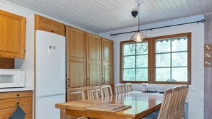 A kitchen with wooden cabinets, a white Bosch refrigerator, a dining table with chairs, and a window with a view of trees.