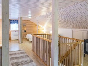 A high-ceilinged room with a wooden floor, a bed, a desk, and a window with curtains.