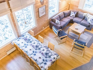 A cozy cabin interior with a sofa, chairs, a dining table, and large windows.