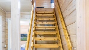 Een houten binnentrap met een leuning, die leidt naar een slaapkamer met een bed en een raam.