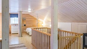 Een ruime slaapkamer op zolder met houten plafond, een bed, nachtkastje en raam met patroongordijnen.