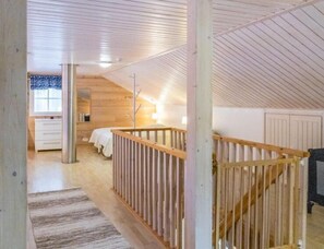 Cozy attic retreat with a high ceiling, wooden beams, and a window with a patterned curtain.
