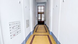 Ein langer, schmaler Korridor mit weißen Wänden, einem Holzboden mit gelben und roten Fliesen und einem großen Fenster am Ende.