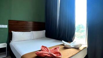 A hotel room with a bed, a window with curtains, and a towel on the bed.