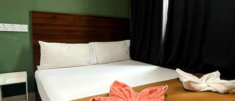 A hotel room with a bed, a nightstand, a brown throw blanket, and a pink towel.