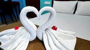 Habitación de hotel con una cama, una mesa marrón y dos toallas dispuestas en forma de cisnes con flores rojas.