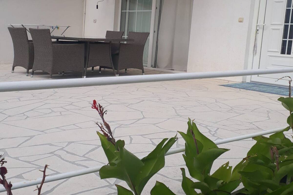 Une terrasse avec une table et des chaises, une porte blanche et un balcon doté d’une balustrade.