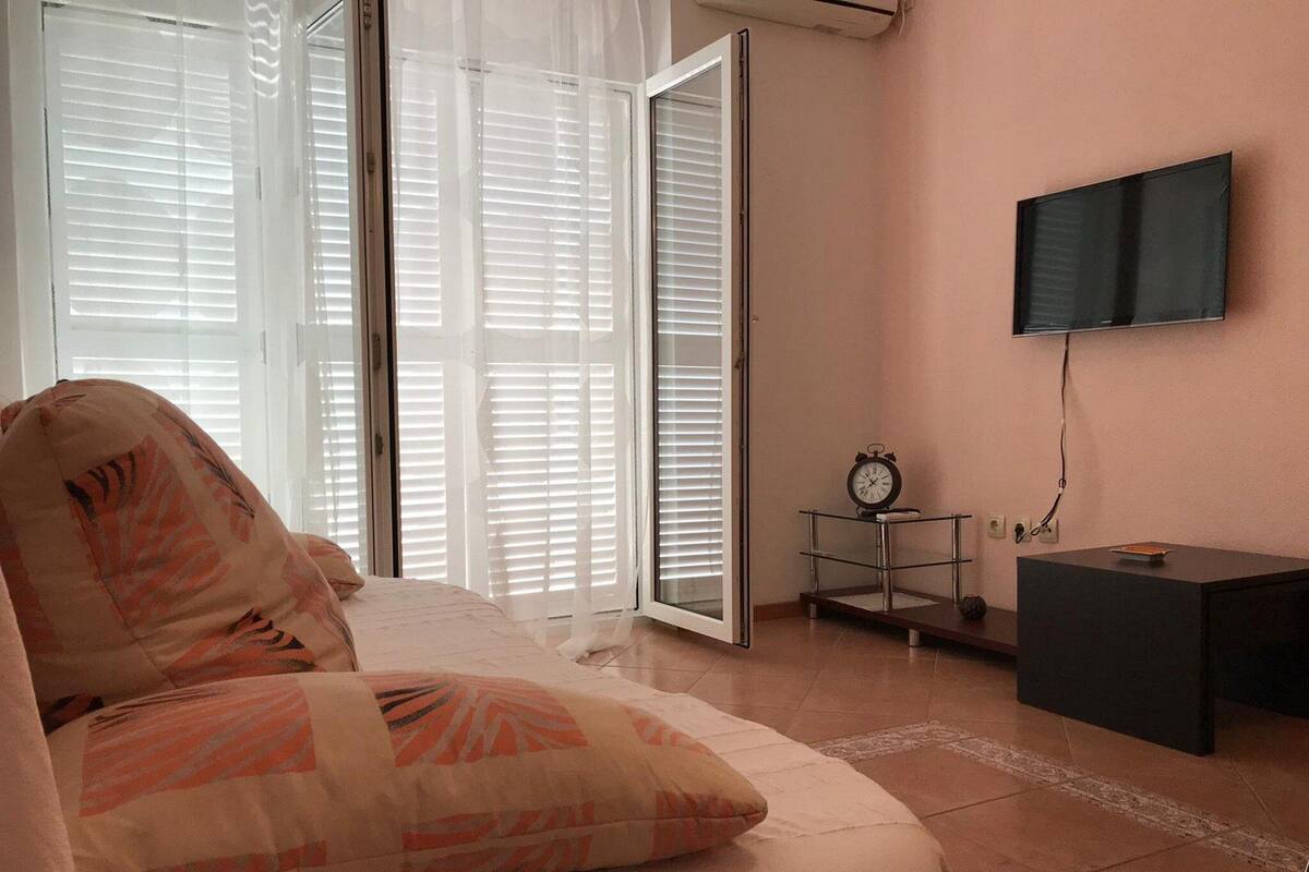 Une chambre à coucher avec un lit, un téléviseur fixé au mur, une petite table avec une horloge et une porte-fenêtre coulissante donnant sur un balcon.
