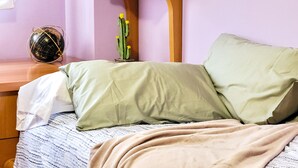 A bed with a patterned bedspread, a beige blanket, and a wooden nightstand with a globe and a cactus decoration. - Apartment in Albacete center (Albacete)