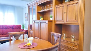 A dining area with a wooden table, chairs, and a red sofa. There are cabinets with glass doors and a shelf with wine glasses. - Apartment in Albacete center (Albacete)