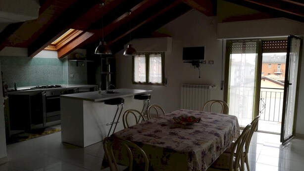 A compact kitchen with a central island, a dining area with a table and chairs, and a view of the outside through a door. - San Lazzaro 81 Mansarda (Andora)
