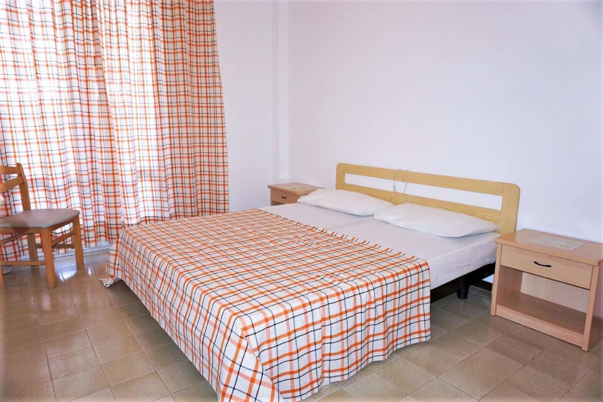 Ein Schlafzimmer mit einem Bett, einem Nachttisch, einem Sessel und einem Fenster mit Vorhängen.