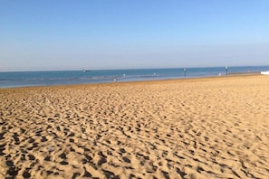 A sandy beach with footprints, a clear sky, and a calm sea.