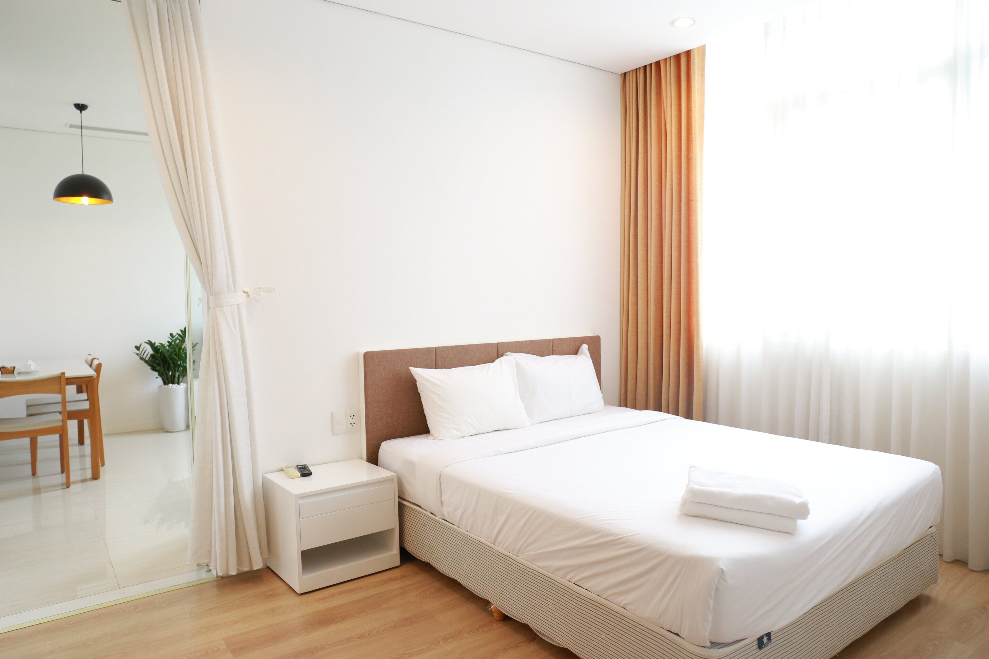 A modern hotel room with a large bed, a bedside table, a small desk, and a potted plant.