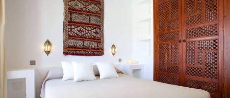 A bedroom with a bed, two bedside tables, a wall-mounted tapestry, and a wooden door with intricate lattice design.