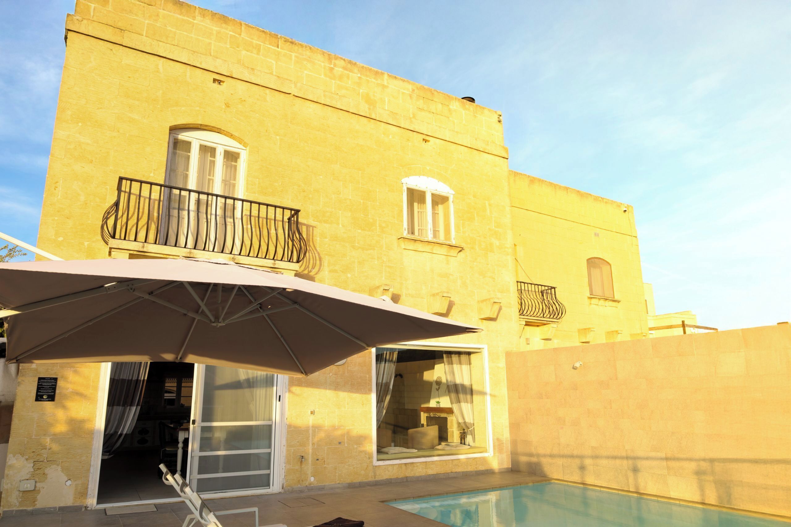Ein Gebäude mit Swimmingpool, einer überdachten Terrasse mit Sonnenschirm und einer Tür zu einem Innenbereich.