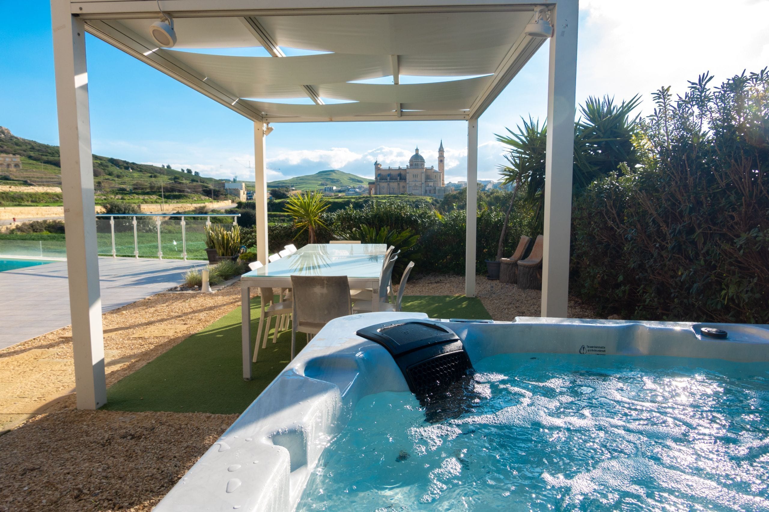 A hot tub with a view of a castle, surrounded by greenery and a covered patio area.
