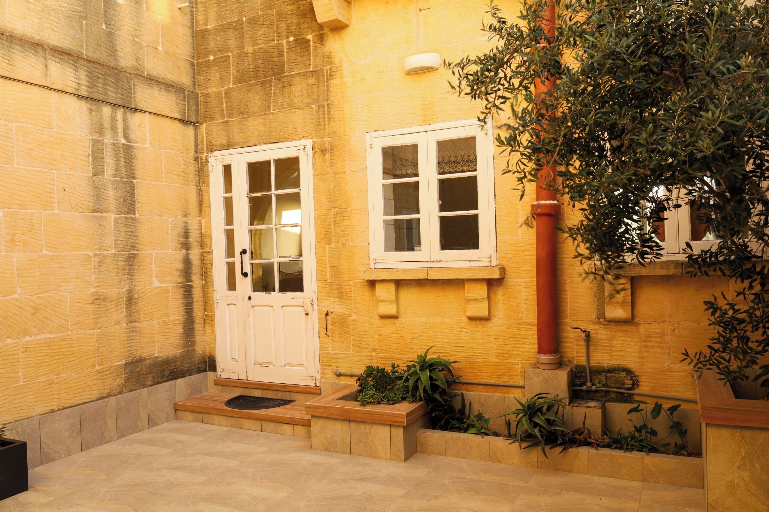 A courtyard with a stone wall, a white door, a window, and potted plants.