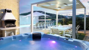 A hot tub with a grill, outdoor seating, and a covered area with umbrellas. - Twilight Holiday Home (Għasri)