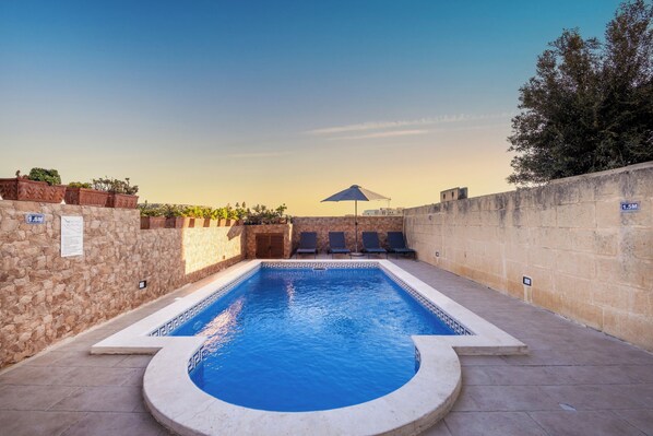 A swimming pool with a sunshade, lounge chairs, and stone walls.