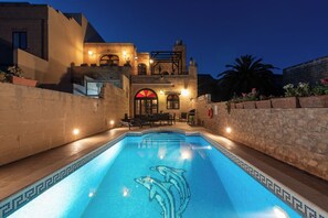 Ein Pool mit Delphinmotiven, eine Steinmauer und ein Gebäude mit Balkon und Beleuchtung.
