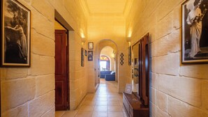 Un couloir aux murs de pierre, orné de tableaux encadrés et doté d’une porte en bois.