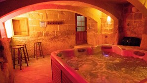 A stone-walled room with a hot tub, wooden stools, and a door. - Villeleynah Holiday Home (Gozo)