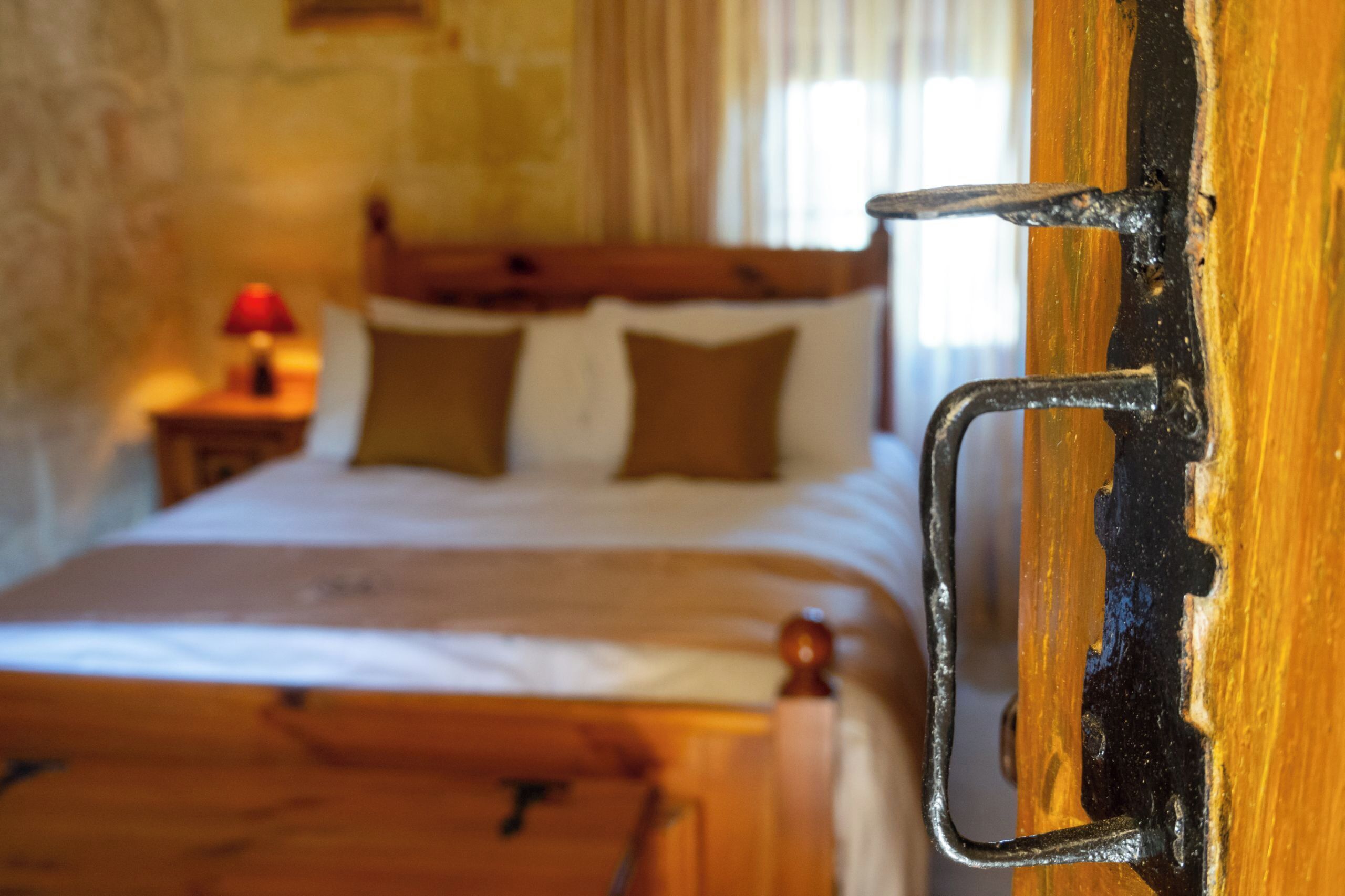 Une chambre à coucher avec un lit en bois, une table de chevet avec une lampe et une porte dotée d’une poignée en métal.