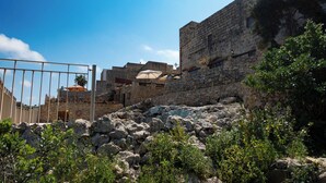 A stone building with a gate, surrounded by greenery and rocks. - Villeleynah Holiday Home (Gozo)