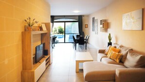 En moderne stue med et fladskærms-tv, en sofa, et sofabord og et spiseområde med stole og et bord.