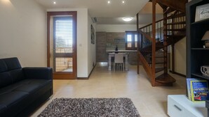 A modern living room with a black sofa, a patterned rug, and a staircase leading to a kitchen area with a dining table. - GetawayNpetto Holiday Home (Ghajnsielem)