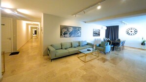 A spacious living area with a sofa, a coffee table, and a dining set. There are two paintings on the wall and a large clock. - Hygge Holiday Home (Ix-Xagħra)