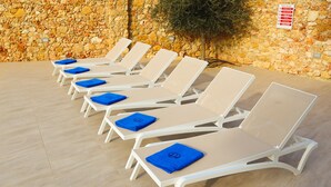 A row of white lounge chairs with blue cushions, arranged against a stone wall. - Hygge Holiday Home (Ix-Xagħra)