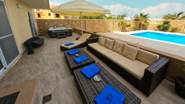 A poolside area with a sofa, lounge chairs, and a hot tub. - Hygge Holiday Home (Ix-Xagħra)
