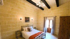 A bedroom with a bed, a nightstand, a wooden wardrobe, and a window with curtains. - Centre Island Holiday Home (Ir-Rabat Għawdex)