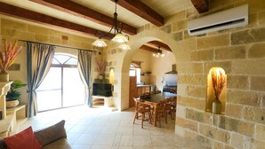 A spacious living area with a stone fireplace, wooden beams, a dining table, and a TV. - Centre Island Holiday Home (Ir-Rabat Għawdex)